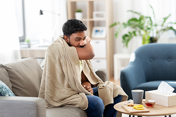 Image showing sick young man in blanket coughing at home