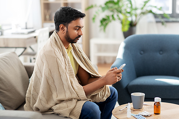 Image showing sick young man in blanket with smartphone at home