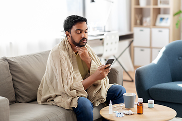 Image showing sick young man in blanket with smartphone at home