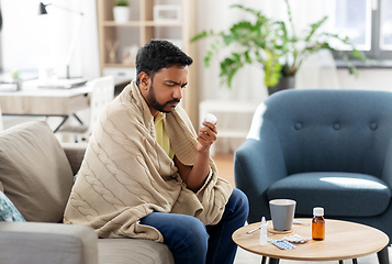 Image showing sad sick man in blanket with medicine at home