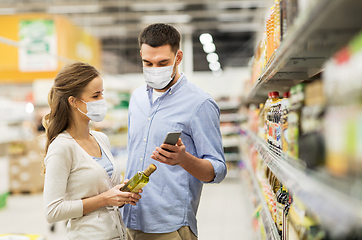 Image showing couple in masks with phone and olive oil at store