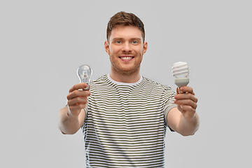 Image showing smiling young man comparing different light bulbs