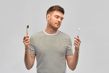 Image showing man comparing wooden and plastic toothbrush