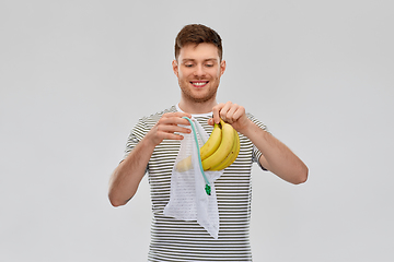 Image showing smiling man putting bananas into reusable net bag