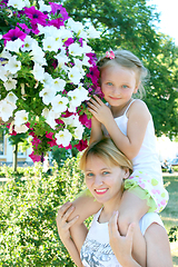 Image showing daughter sitting on her mother and many flowers in the city park