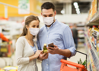 Image showing couple in masks with phone and olive oil at store