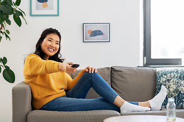 Image showing asian woman with tv remote sitting on sofa at home