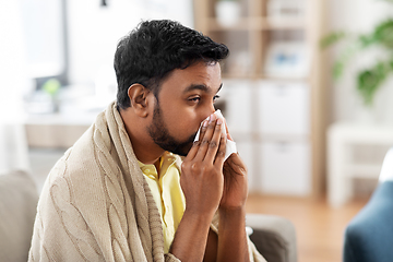 Image showing sick man blowing nose in paper tissue at home