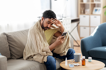 Image showing sick young man in blanket with smartphone at home