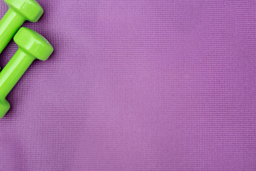 Image showing Ladie's dumbbells over purple fitness mat, top view.