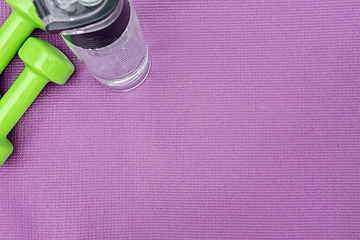 Image showing Ladie's dumbbells and water bottle over purple fitness mat, top view.