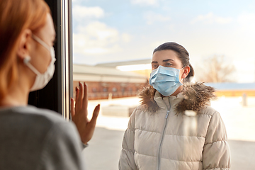 Image showing woman in mask looking to friend through window