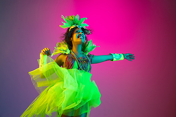 Image showing Beautiful young woman in carnival and masquerade costume on gradient studio background in neon light