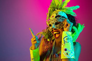 Image showing Beautiful young woman in carnival and masquerade costume on gradient studio background in neon light