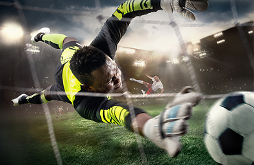 Image showing African male soccer or football player, goalkeeper in action at stadium. Young man catching ball, training, protecting goals in motion.