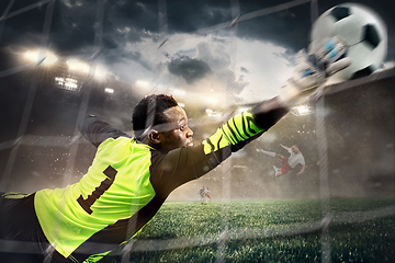 Image showing African male soccer or football player, goalkeeper in action at stadium. Young man catching ball, training, protecting goals in motion.