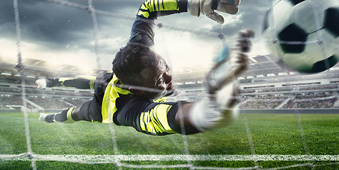 Image showing African male soccer or football player, goalkeeper in action at stadium. Young man catching ball, training, protecting goals in motion.