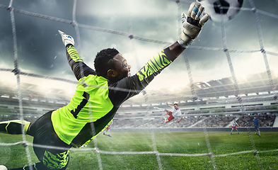 Image showing African male soccer or football player, goalkeeper in action at stadium. Young man catching ball, training, protecting goals in motion.