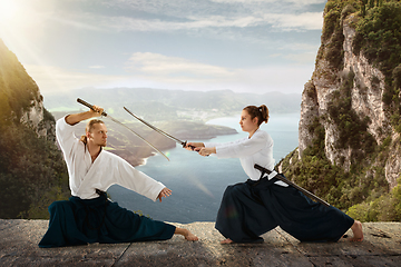 Image showing Man and woman, teacher fighting Aikido, training martial arts on meadow in front of lake and mountains