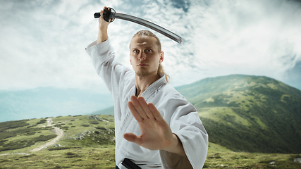 Image showing Young man, teacher fighting Aikido, training martial arts on meadow in front mountains