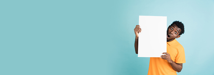 Image showing Young African man with blank sheet of paper isolated over blue studio background.