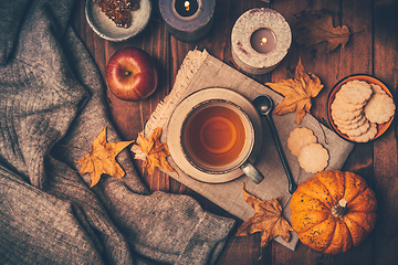 Image showing Hot tea with cookies, apple and fall foliage and pumpkins on wooden background