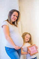 Image showing Beautiful pregnant woman with daughter standing near a wall at home