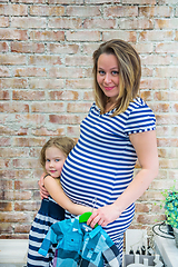 Image showing Beautiful pregnant woman with daughter near the wall