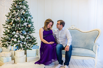 Image showing Pregnant woman in an ultraviolet dress with husband sitting near Christmas tree
