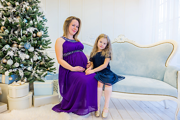 Image showing Beautiful pregnant woman in an ultraviolet dress sitting with daughter