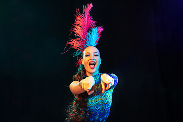 Image showing Beautiful young woman in carnival and masquerade costume in colorful neon lights on black background