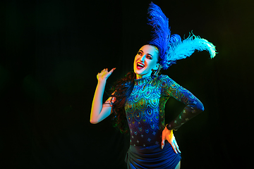 Image showing Beautiful young woman in carnival and masquerade costume in colorful neon lights on black background