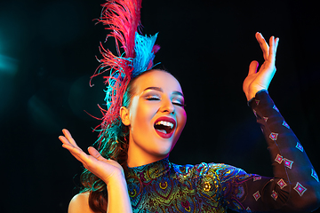 Image showing Beautiful young woman in carnival and masquerade costume in colorful neon lights on black background