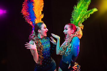 Image showing Beautiful young women in carnival and masquerade costume in colorful neon lights on black background