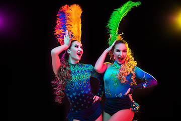 Image showing Beautiful young women in carnival and masquerade costume in colorful neon lights on black background