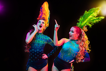 Image showing Beautiful young women in carnival and masquerade costume in colorful neon lights on black background