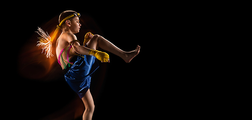 Image showing Little boy exercising thai boxing on black background. Fighter practicing, training in martial arts in action, motion. Evolution of movement, catching moment.