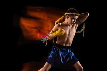 Image showing Little boy exercising thai boxing on black background. Fighter practicing, training in martial arts in action, motion. Evolution of movement, catching moment.