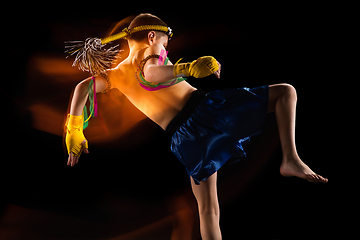 Image showing Little boy exercising thai boxing on black background. Fighter practicing, training in martial arts in action, motion. Evolution of movement, catching moment.