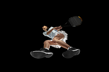 Image showing Female professional tennis player in action, motion isolated on black background, look from the bottom. Concept of sport, movement, energy and dynamic.