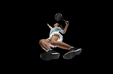 Image showing Female professional tennis player in action, motion isolated on black background, look from the bottom. Concept of sport, movement, energy and dynamic.