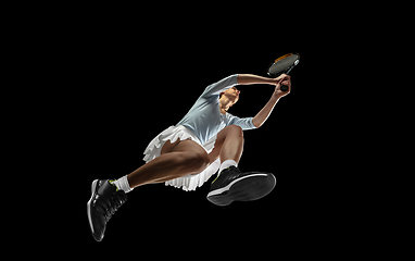 Image showing Female professional tennis player in action, motion isolated on black background, look from the bottom. Concept of sport, movement, energy and dynamic.