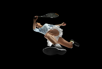 Image showing Female professional tennis player in action, motion isolated on black background, look from the bottom. Concept of sport, movement, energy and dynamic.