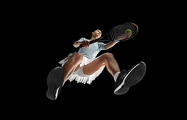 Image showing Female professional tennis player in action, motion isolated on black background, look from the bottom. Concept of sport, movement, energy and dynamic.