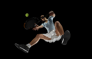 Image showing Female professional tennis player in action, motion isolated on black background, look from the bottom. Concept of sport, movement, energy and dynamic.