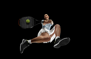 Image showing Female professional tennis player in action, motion isolated on black background, look from the bottom. Concept of sport, movement, energy and dynamic.