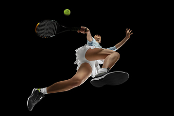 Image showing Female professional tennis player in action, motion isolated on black background, look from the bottom. Concept of sport, movement, energy and dynamic.