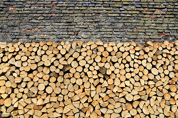 Image showing Stack of firewood against old weathered brick wall