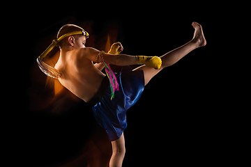 Image showing Little boy exercising thai boxing on black background. Fighter practicing, training in martial arts in action, motion. Evolution of movement, catching moment.