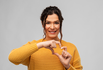 Image showing smiling young woman making hand heart gesture